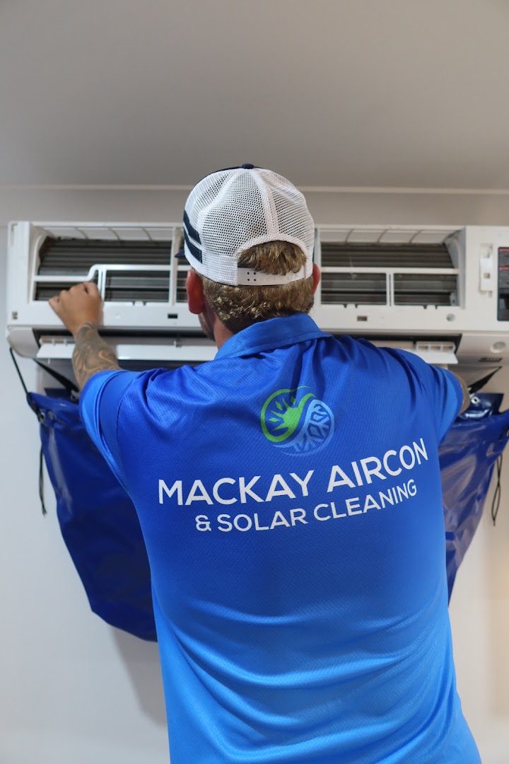 A worker in a branded shirt lifting the cover off a wall-mounted split system