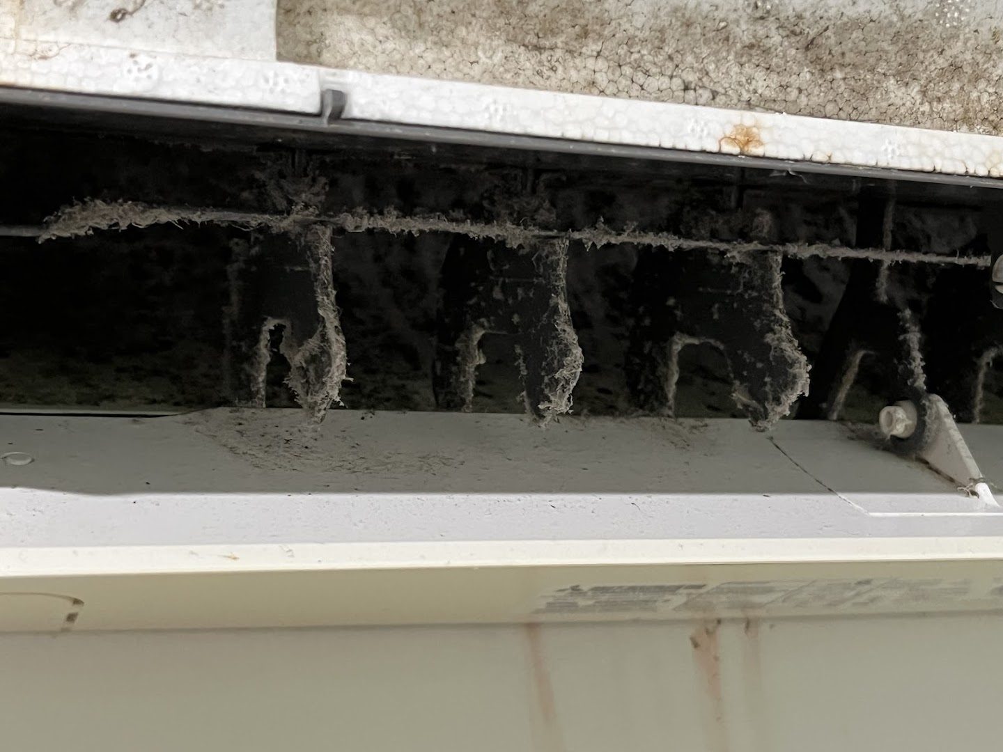 A close view inside an air conditioner head showing heavy build-up along the vanes