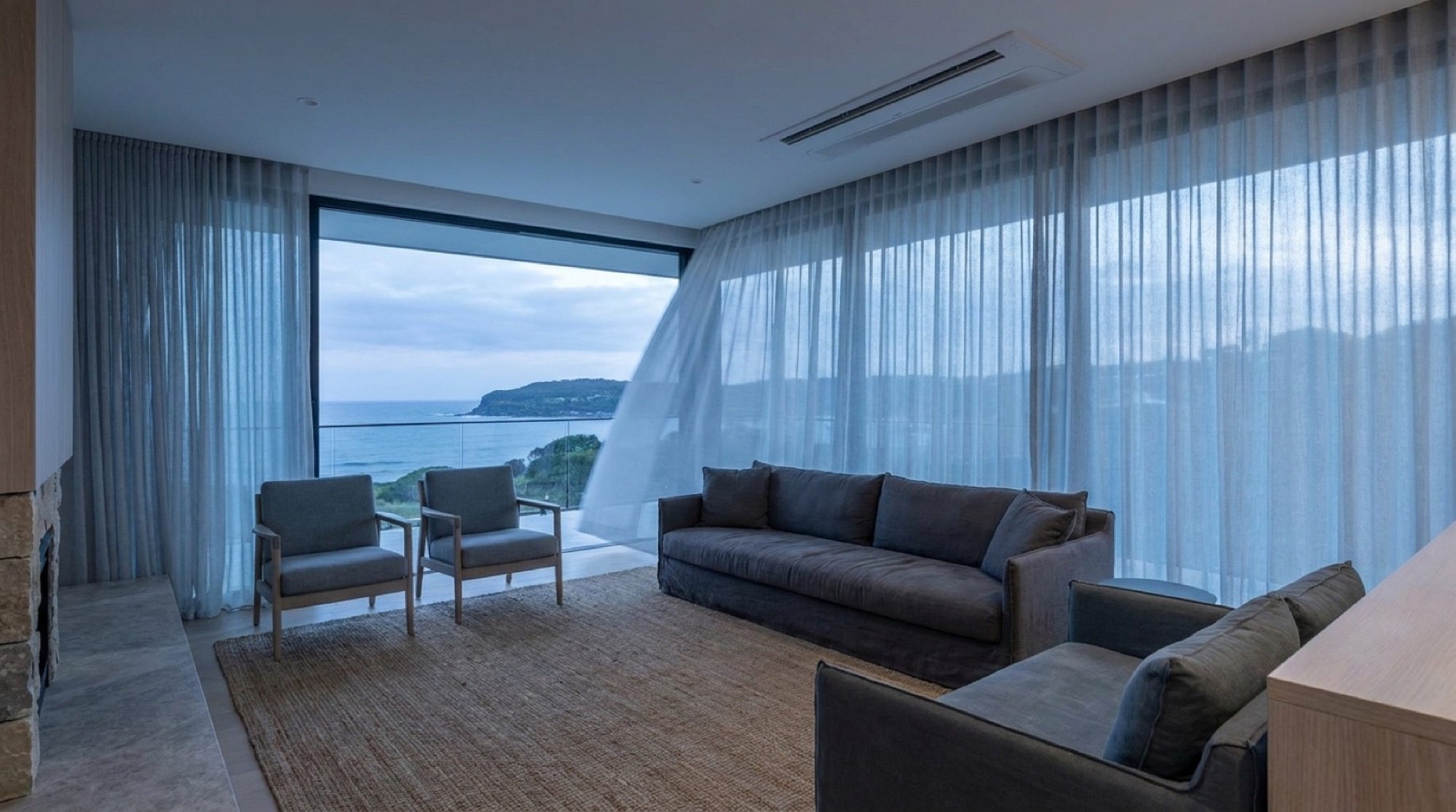 A calm living room with a wall-mounted split system and light through sheer curtains