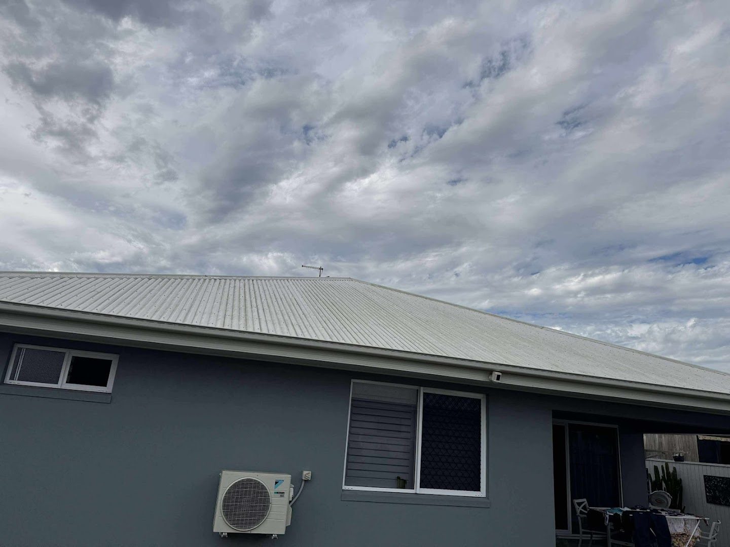 An outdoor air conditioning unit on the wall of a home under a heavy sky