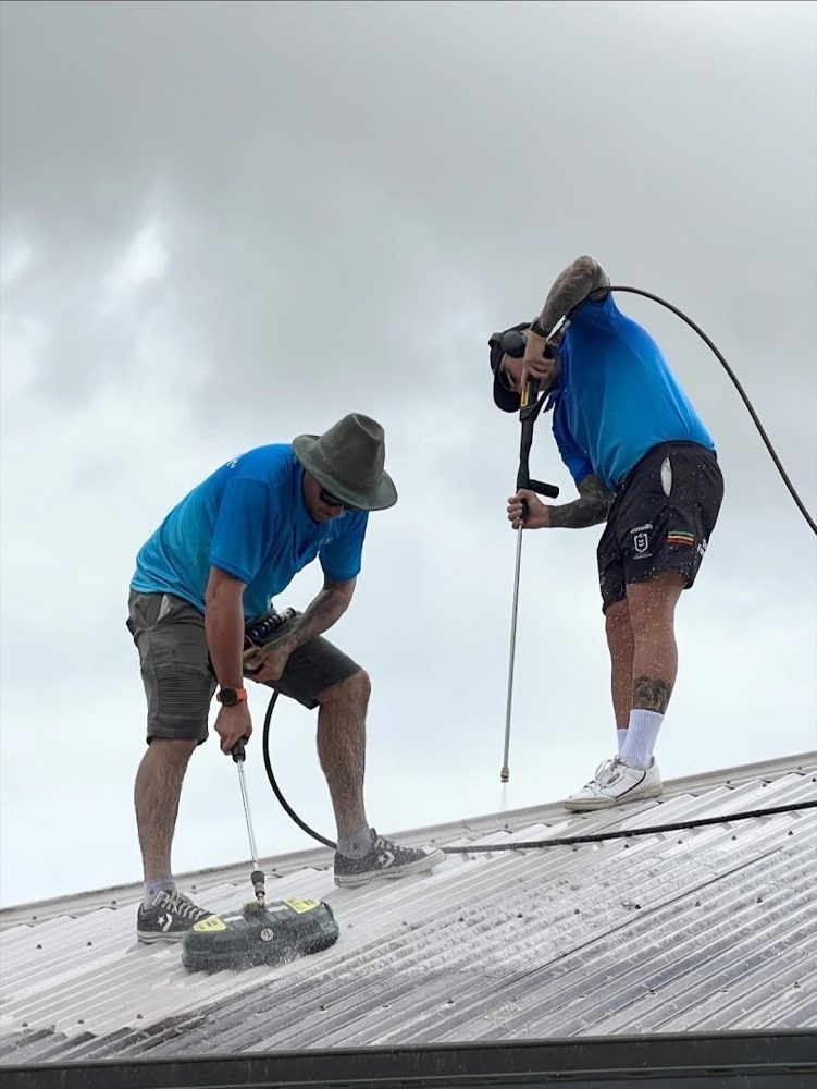 Two workers washing a metal roof with a surface cleaner and a lance