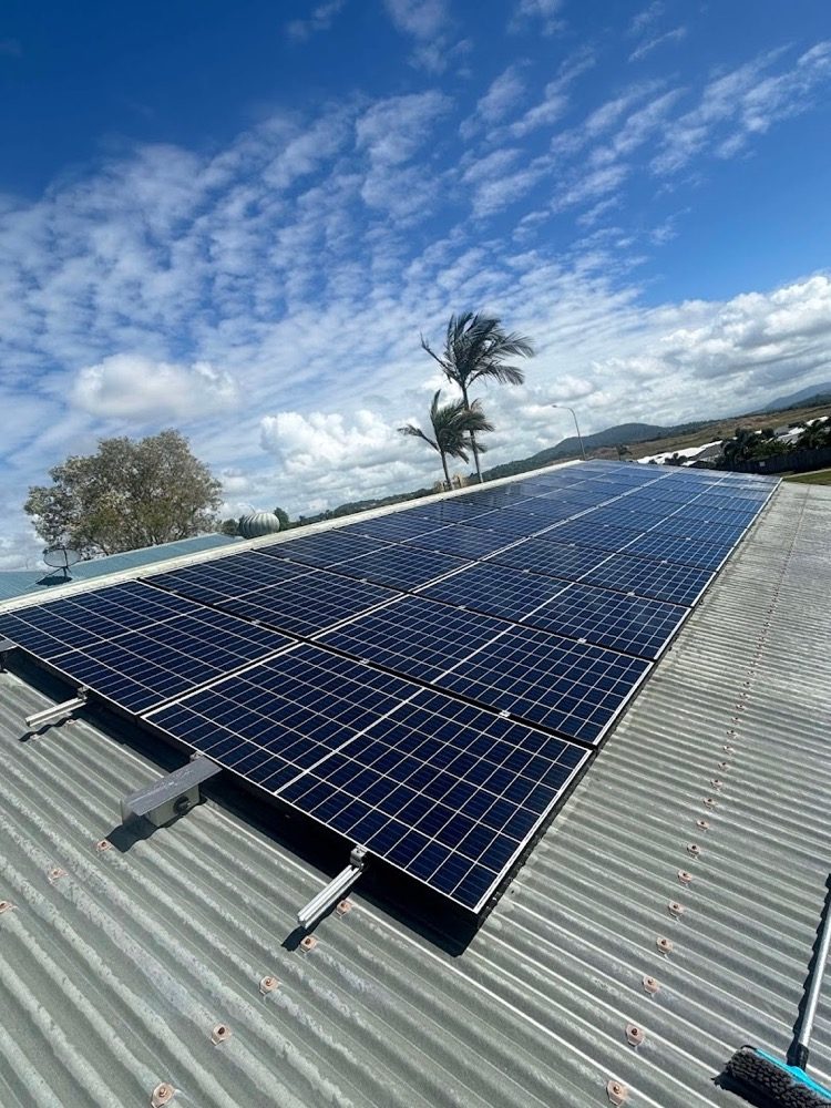 A rooftop solar array on a metal roof under a bright sky with a palm tree behind