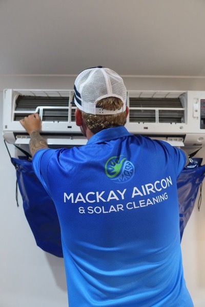 A worker in a branded shirt lifting the cover off a wall-mounted split system