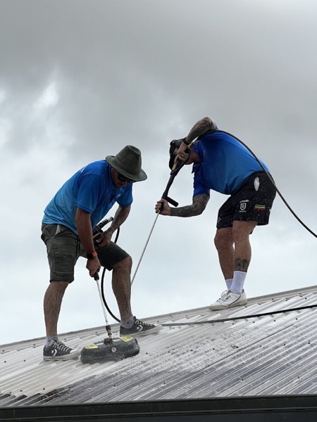 Two workers washing a metal roof with a surface cleaner and a lance