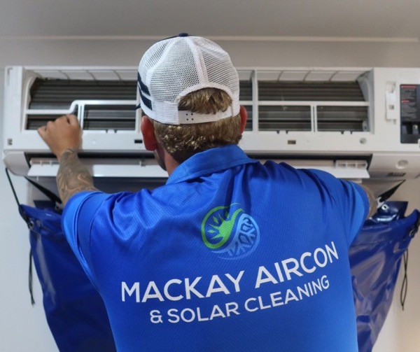 A worker in a branded shirt reaching into a split system with a catch bag fitted