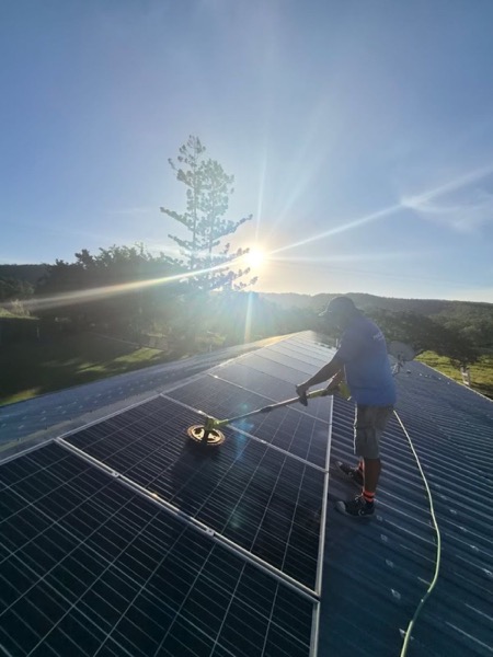 A worker washing a rooftop solar array on a metal roof