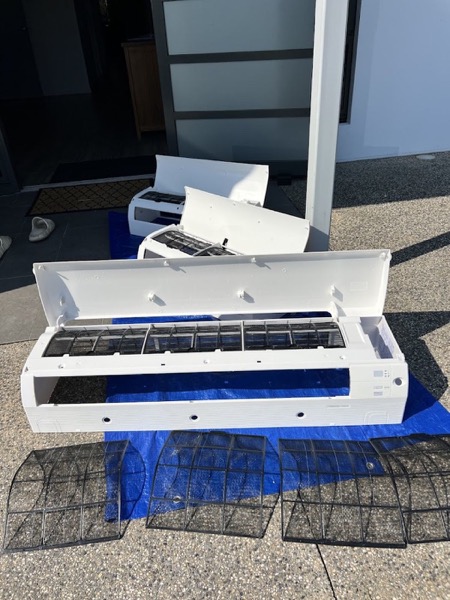 An air conditioner head opened up on a drop sheet beside its filters