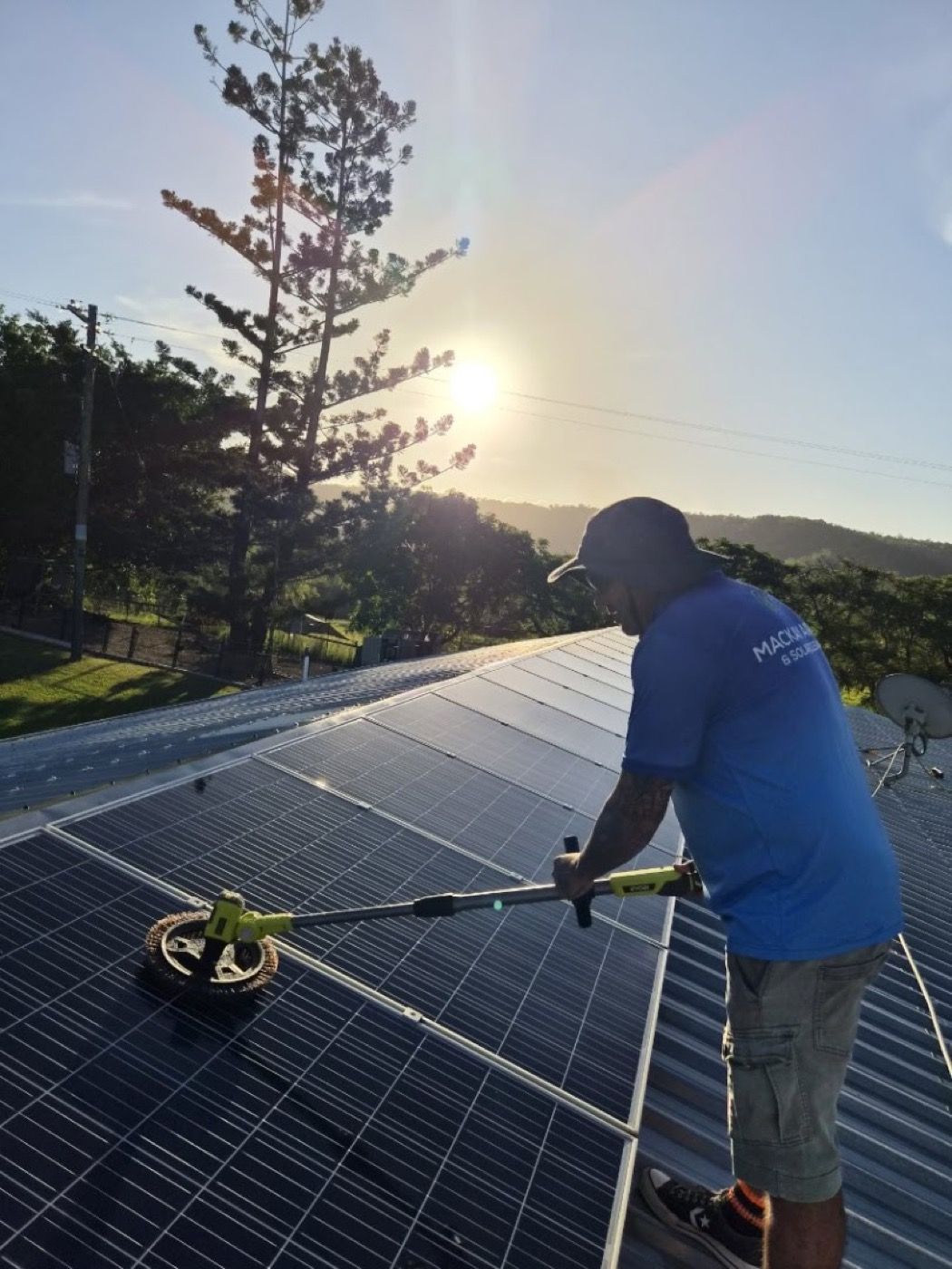 A worker brushing a rooftop solar array at sunrise