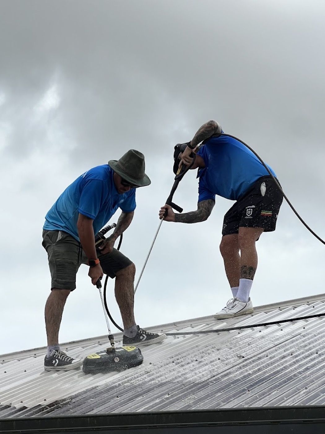 Two workers washing a metal roof with a pressure lance