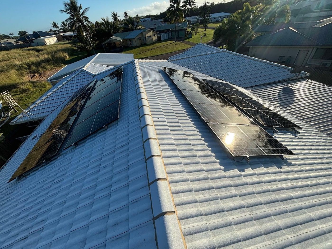 Solar panels on a tiled roof with houses and palms behind